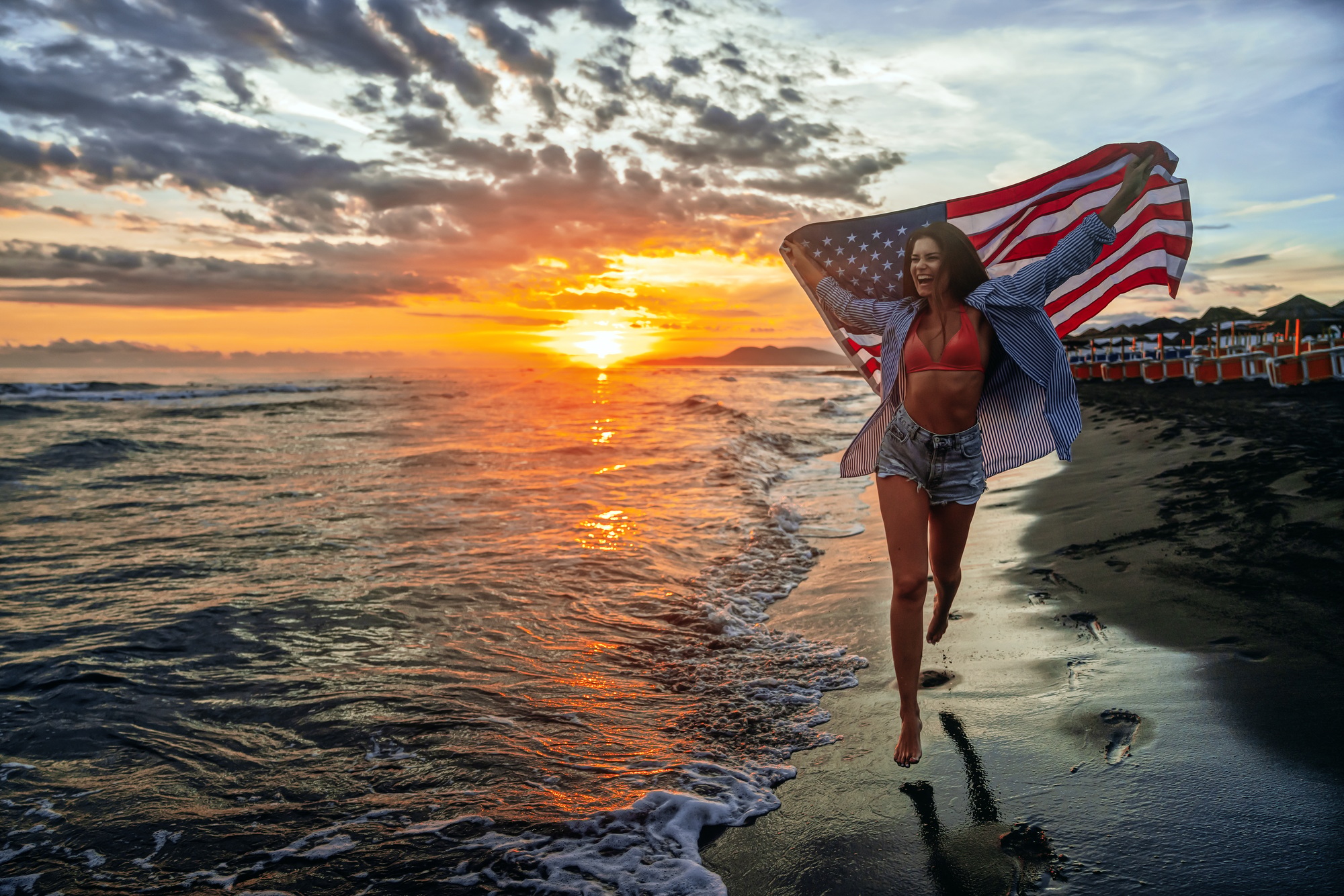 Happy woman holding american USA flag and running on the beach. Independence Day, travel concept